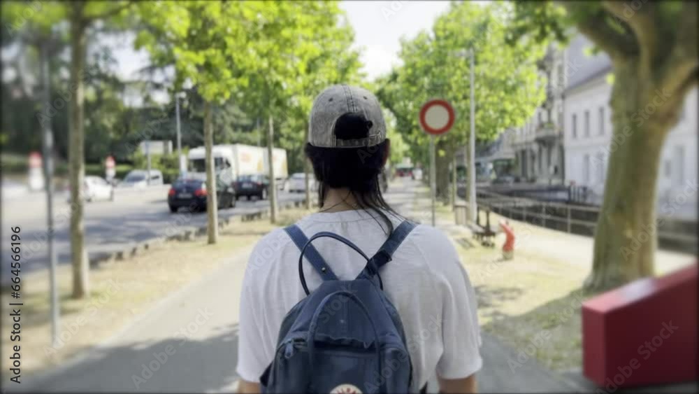 Woman Walking Alone on a Sunny Day Along a Tree-Lined Sidewalk Next to a Busy Avenue and a Grand Old Building, Wearing a Cap and Carrying a Backpack on Her Back Woman Walking Alone on a Sunny Day Along a Tree-Lined Sidewalk Next to a Busy Avenue and a Grand Old Building, Wearing a Cap and Carrying a Backpack on Her Back