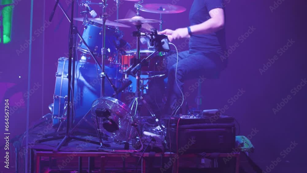 Close-up of a drummer behind a blue drum kit. A man rhythmically playing with his hands and feet. Side view. Drummer playing on stage