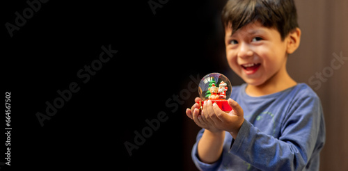 A boy with a sweet smile looking at the camera and holding a Christmas snow globe in his hands. Copy space.