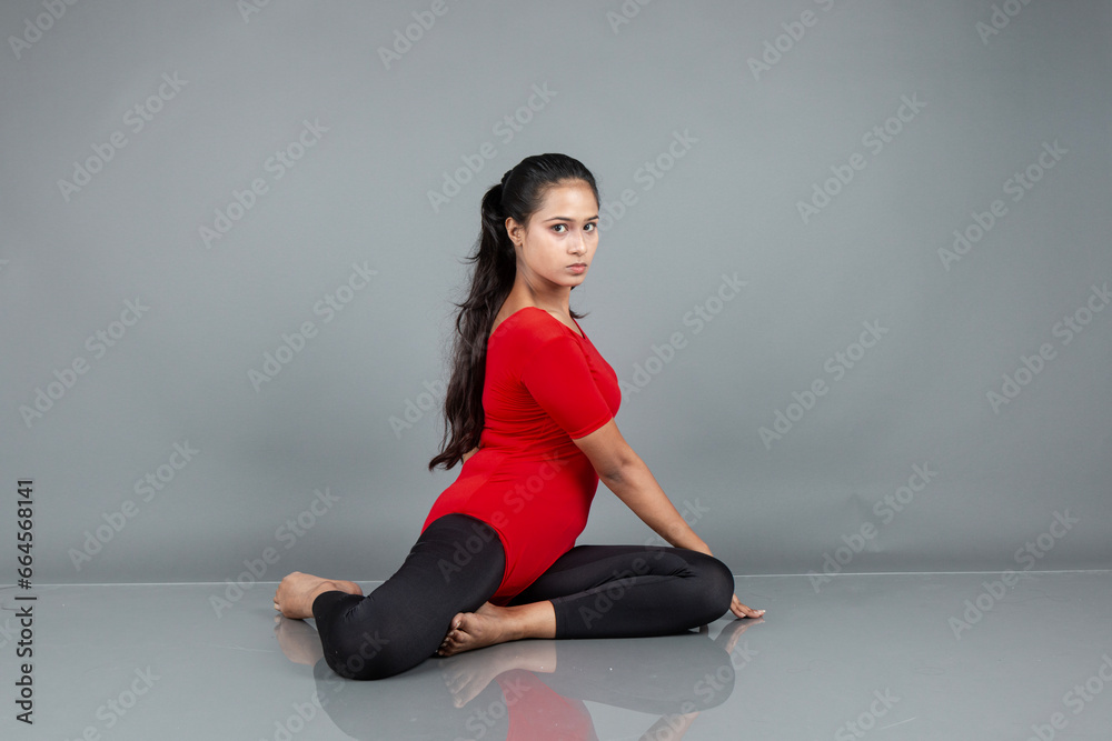 Fototapeta premium Healthy young woman in red t-shirt and black leggings doing yoga and stretching exercises isolated on grey background
