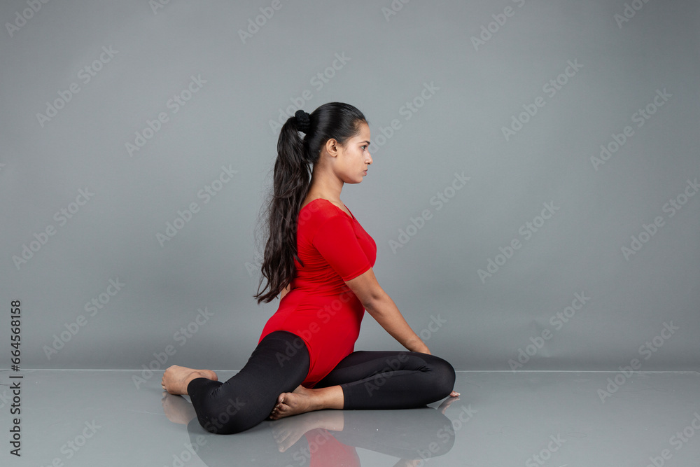 Fototapeta premium Healthy young woman in red t-shirt and black leggings doing yoga and stretching exercises isolated on grey background