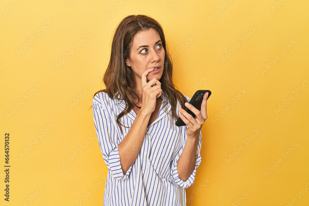 Middle aged woman using mobile phone in a yellow studio setting Middle aged woman using mobile phone in a yellow studio setting