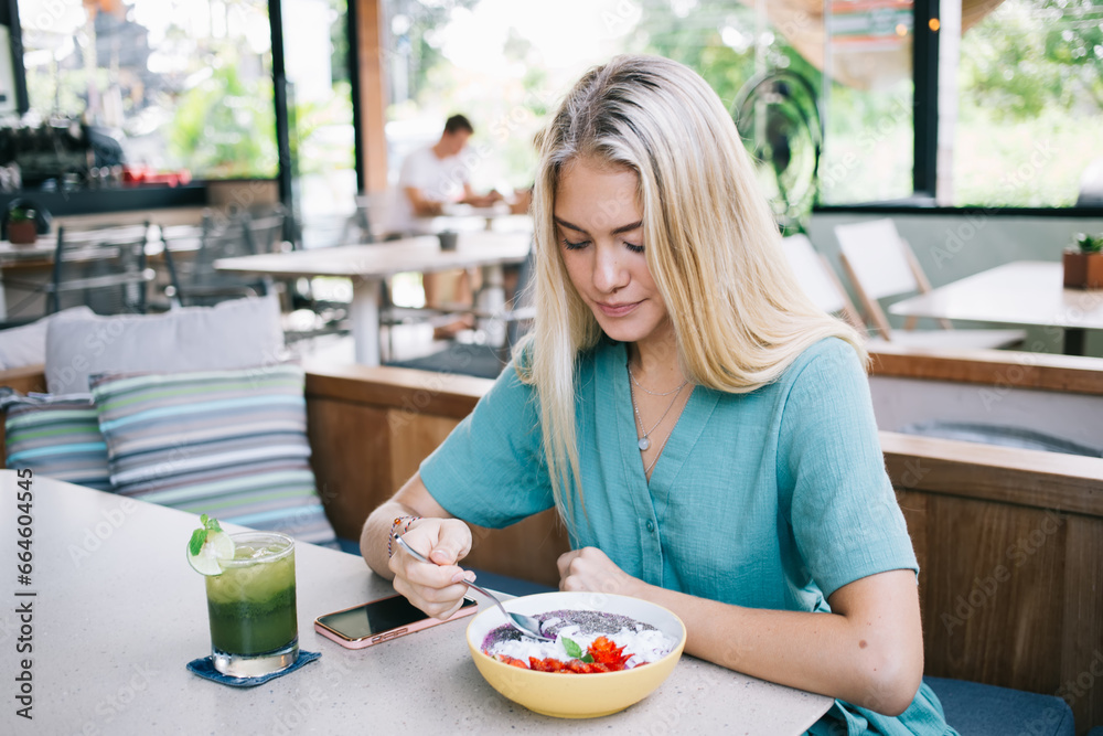Caucasian female ordered bowl with fresh delicious meal during lunch time in local cafe interior with organic food, woman eating vegan delicious meal for breakfast enjoying detox nutrition