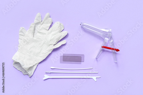 Medical gloves with gynecological speculum and pap smear test tools on lilac background photo