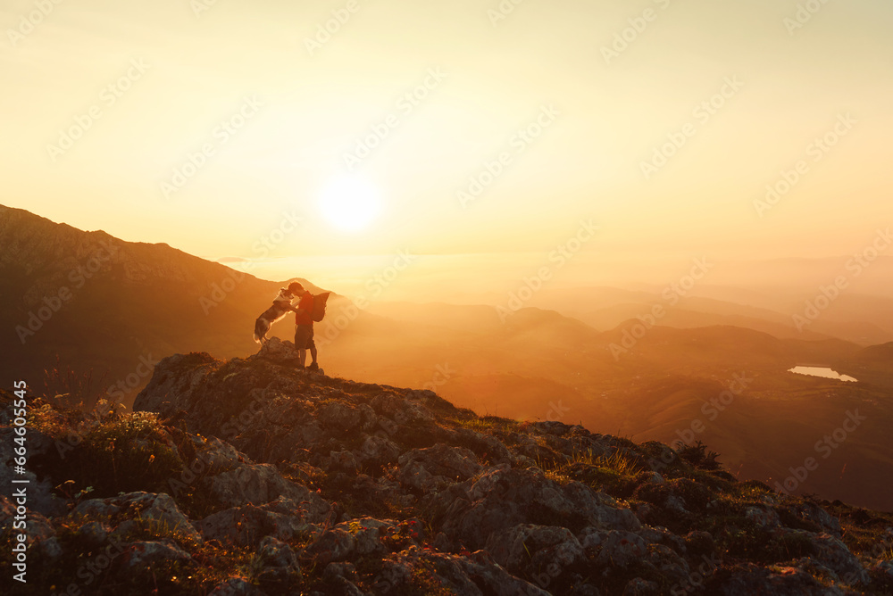 Silhouette of a mountaineer man with his dog in a gesture of complicity and unity while hiking in the mountains at sunset. Traveling with a pet. Sport and adventure.