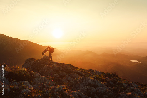 Silhouette of a mountaineer man with his dog in a gesture of complicity and unity while hiking in the mountains at sunset. Traveling with a pet. Sport and adventure.