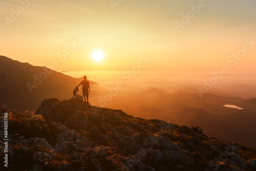 Man on his back with his dog contemplating the sunset in the mountains. Sport, adventure and hiking. traveling with a pet.