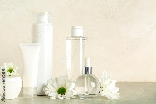 Different cosmetic products and chamomile flowers on table against light background