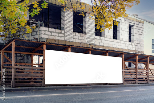 Long information banner with space for mockup placed on wooden scaffolding on city sidewalk with unfinished white brick house in autumn