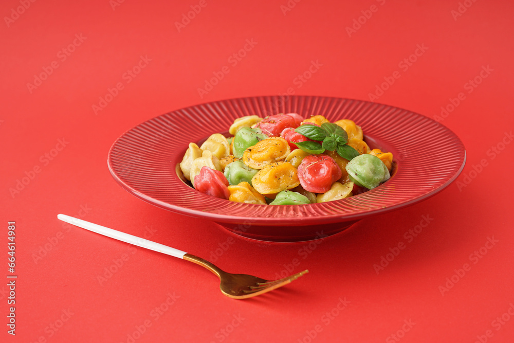 Plate with boiled colorful dumplings and basil on red background Plate with boiled colorful dumplings and basil on red background