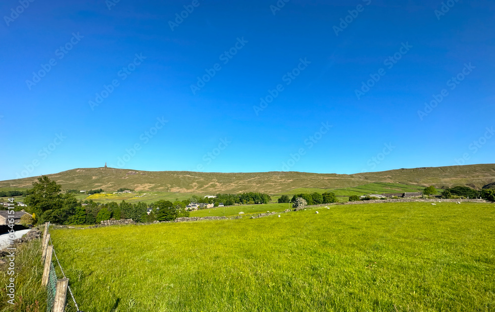 Rural landscape, extensive fields, and distant moorland with, Stoodley Pike set against a blue sky in, Mankinholes, UK