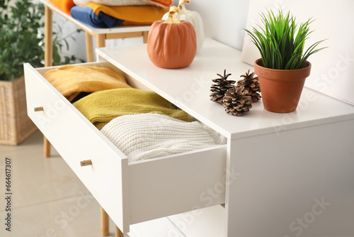 Chest of drawers with warm clothes and autumn decor in room