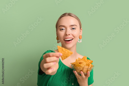 Pretty young woman with nachos on green background