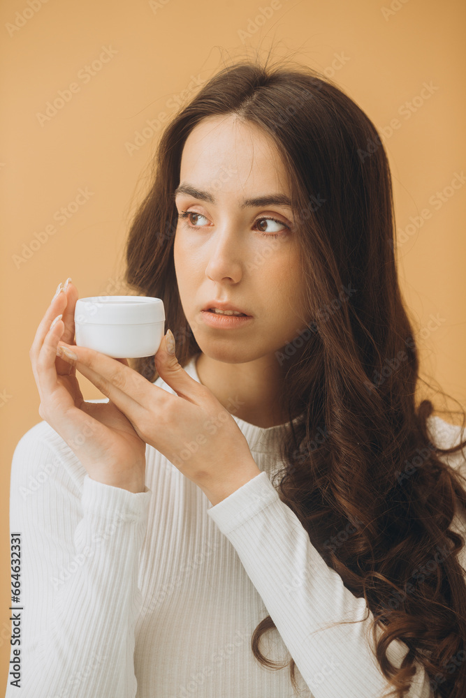 Fashion portrait of a beautiful woman with a bottle of cosmetic cream on a beige pastel background. Fashion portrait of a beautiful woman with a bottle of cosmetic cream on a beige pastel background.