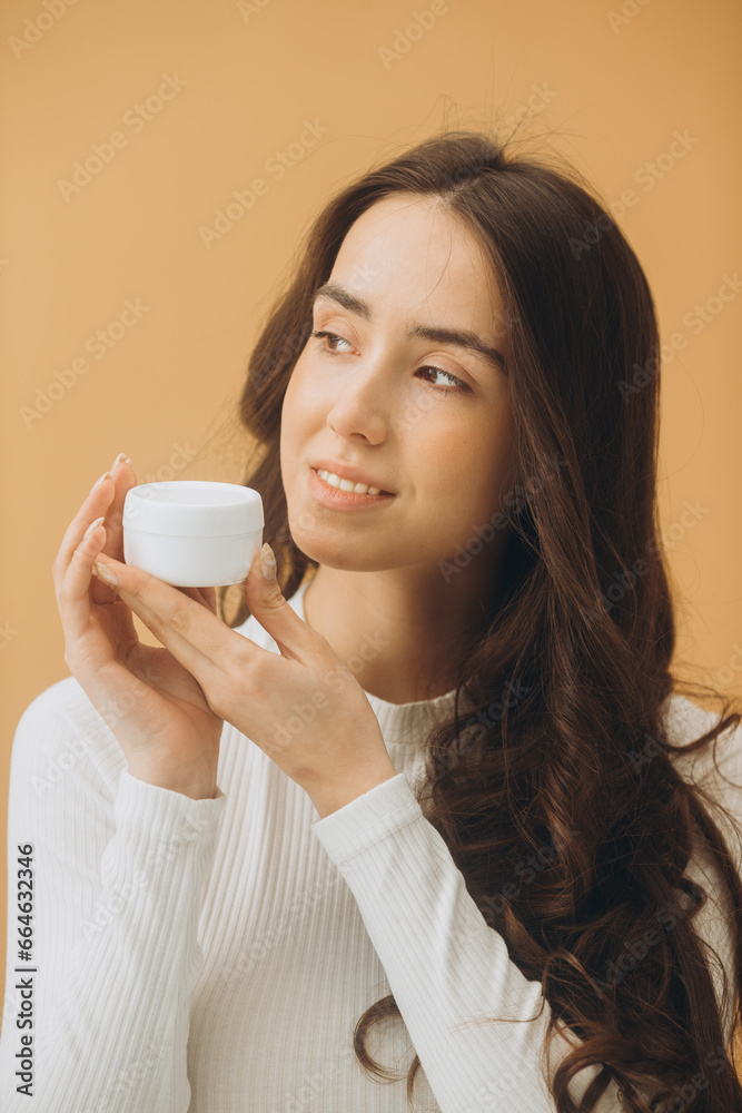 Fashion portrait of a beautiful woman with a bottle of cosmetic cream on a beige pastel background. Fashion portrait of a beautiful woman with a bottle of cosmetic cream on a beige pastel background.