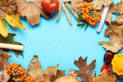 Frame made of autumn leaves with candles, rowan and ears of wheat on blue background