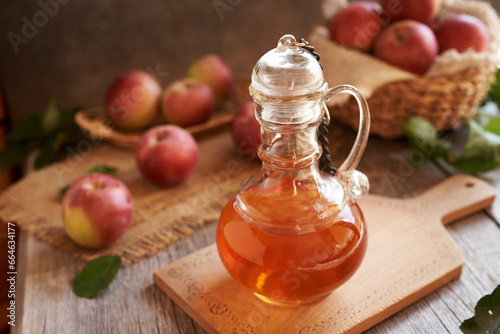 A jug of apple cider vinegar with fresh apples on a table