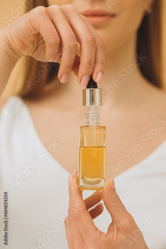 Skin care. Beauty portrait of woman holding dropper bottle isolated on beige background. Close up photo.