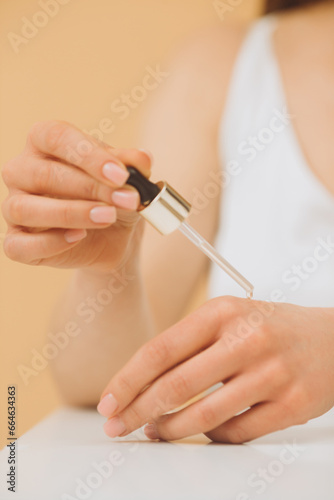 Cropped photo of a young woman dropping cosmetic oil on the back of her hand.