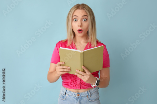 Beautiful young shocked woman with book on blue background