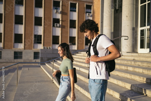 Happy classmates wearing casual clothes leaving college. They are walking down the stairs of the faculty building while talking and laughing