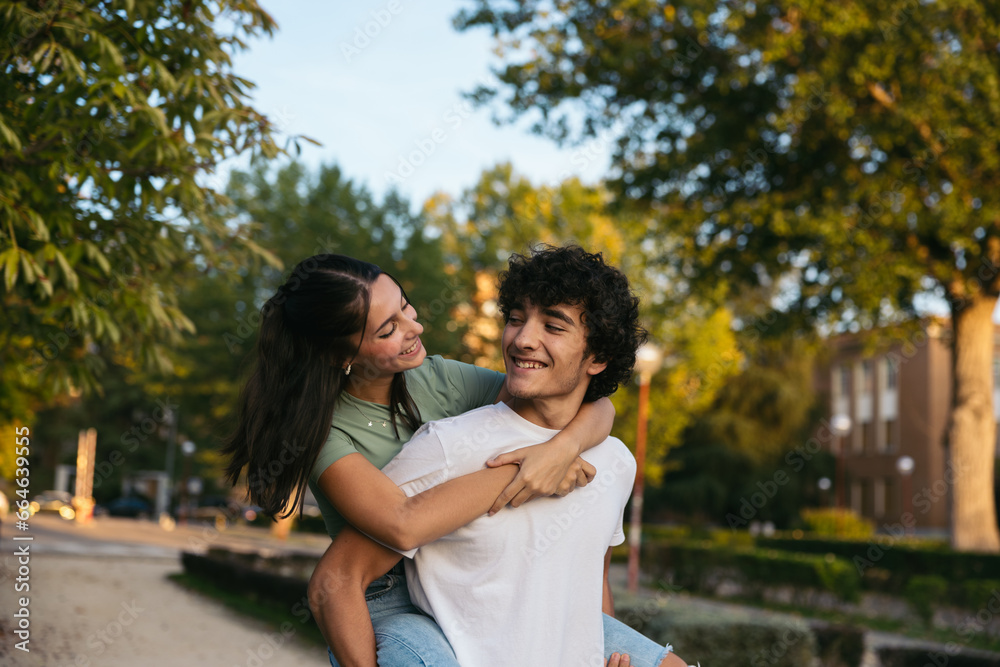 Pair of cute students leaving college. The girl is standing on top of the boy and they are looking at each other and smiling Pair of cute students leaving college. The girl is standing on top of the boy and they are looking at each other and smiling