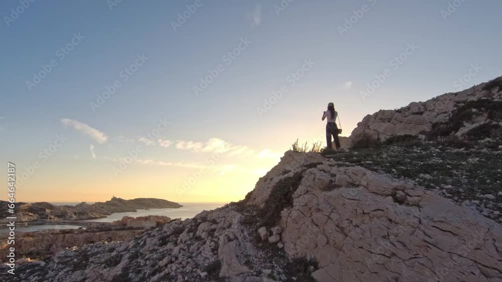 A young Caucasian girl shoots a beautiful sunset on her smartphone overlooking a pier on the island of Friulle in France, a side view with slow motion and tracking to the left. Journey concept. A young Caucasian girl shoots a beautiful sunset on her smartphone overlooking a pier on the island of Friulle in France, a side view with slow motion and tracking to the left. Journey concept.