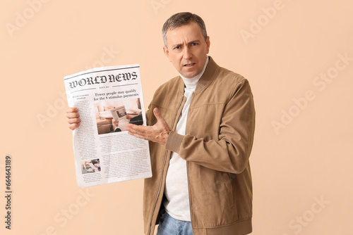 Upset mature journalist with newspaper on beige background