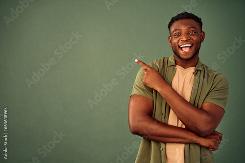 Advertising product. Positive young guy in casual khaki shirt pointing with finger on green background with copy space. Excited african man presenting promo offer or holiday discount in studio. photo