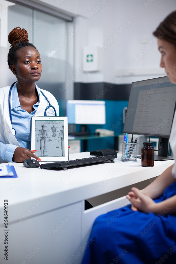 Obraz premium Bone specialist doctor at physical consultation offering anatomy information to patient on tablet using human skeleton figure. Orthopedist providing healthcare diagnosis to woman at appointment