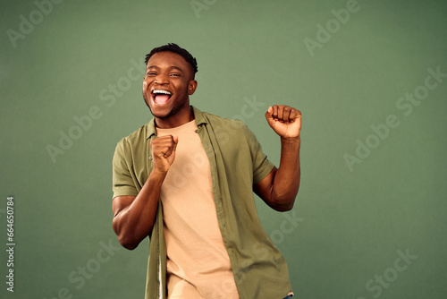 Leisure with fun. Energetic african american gun in casual wear actively dancing with flexible body over green studio background. Joyful young man having fun while perfectly feeling music beat.
