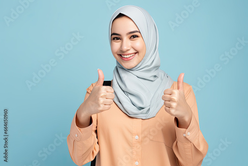 Young smiling happy arabian asian muslim woman in abaya hijab clothes showing thumb up like gesture isolated on plain blue background studio portrait People middle eastern islam religious concept photo