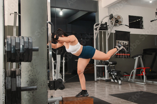 Fitness girl using a machine to do buttock exercises in the gym. © Hugo