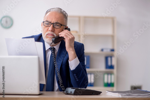 Old male employee talking by phone