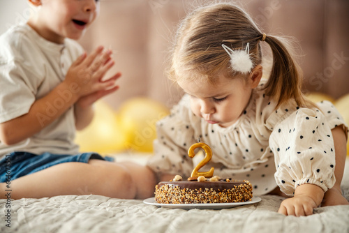A birthday girl makes a wish and blowing candle while her brother is clapping.