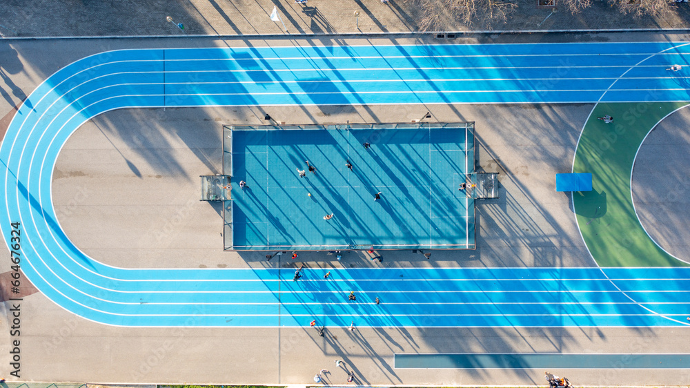 Obraz premium Aerial drone top view of running track mini football soccer field with artificial plastic cover with playing people. Public sport ground in city at sunny summer day drone view