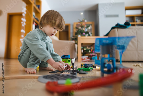 Cute toddler boy playing with wooden train set. Small child having fun with toys. Kid spending time in a cozy living room at home.