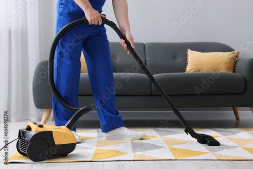 Dry cleaner's employee hoovering carpet with vacuum cleaner in room, closeup