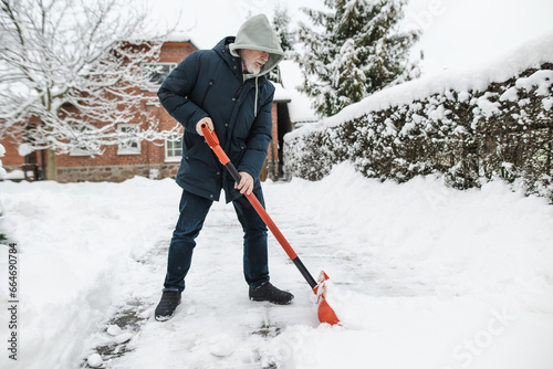 Mature man shoveling snow in a backyard on winter day.