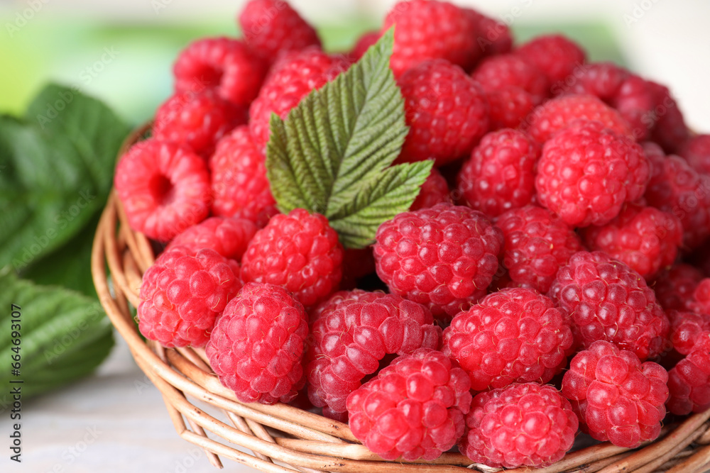 Tasty ripe raspberries and green leaf in basket on table, closeup