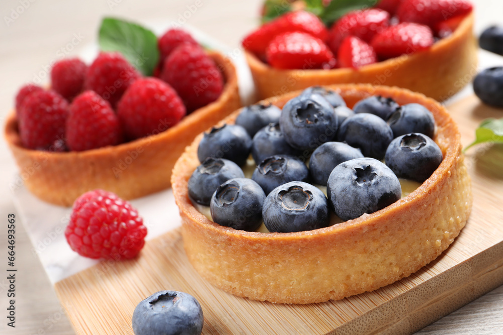 Fototapeta premium Tartlets with different fresh berries on board, closeup. Delicious dessert