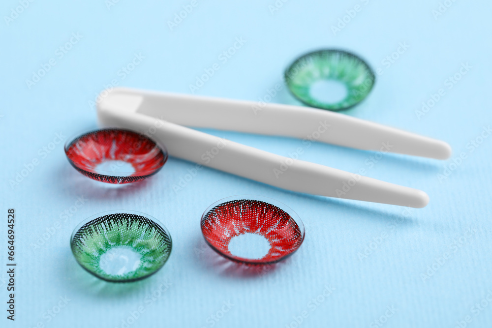 Different color contact lenses and tweezers on light blue background