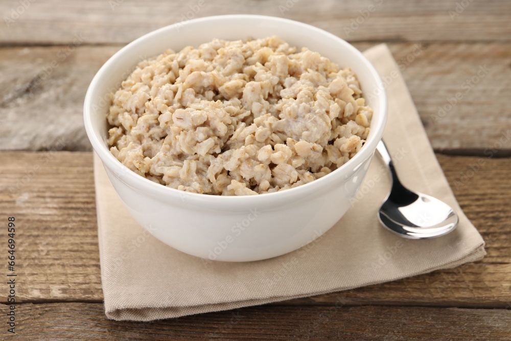 Tasty boiled oatmeal in bowl and spoon on wooden table, closeup Tasty boiled oatmeal in bowl and spoon on wooden table, closeup