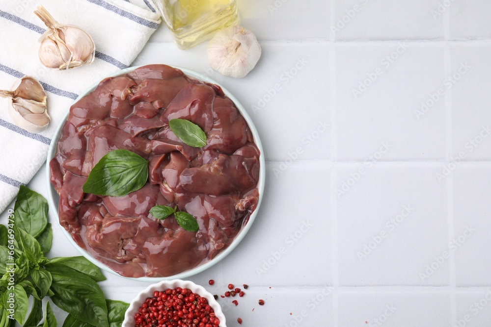 Plate of raw chicken liver with basil and products on white tiled table, flat lay. Space for text
