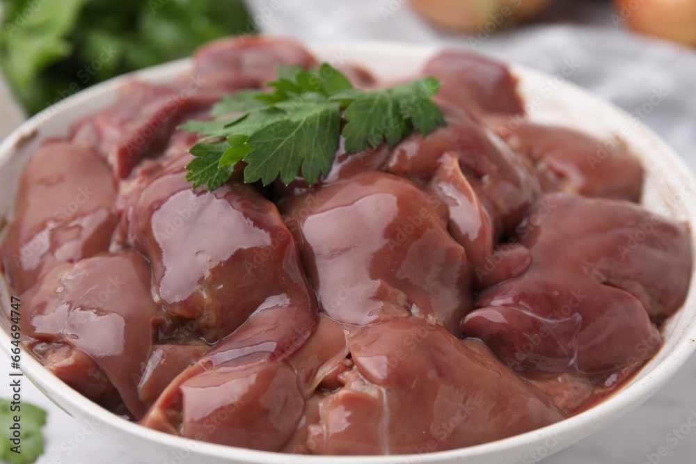 Bowl of raw chicken liver with parsley on white table, closeup