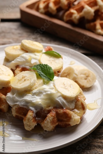 Delicious Belgian waffles with banana and whipped cream on table, closeup