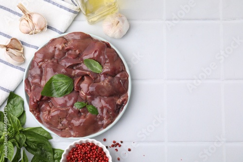 Plate of raw chicken liver with basil and products on white tiled table, flat lay. Space for text