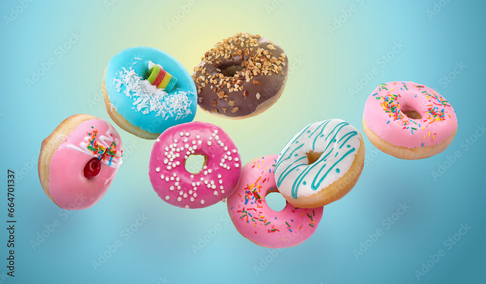 Obraz premium Different tasty donuts falling on color background. Banner design