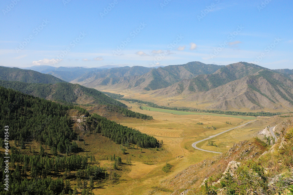 View from the top of a picturesque valley surrounded by mountains from fragments of an asphalt road that turns sharply to the right.