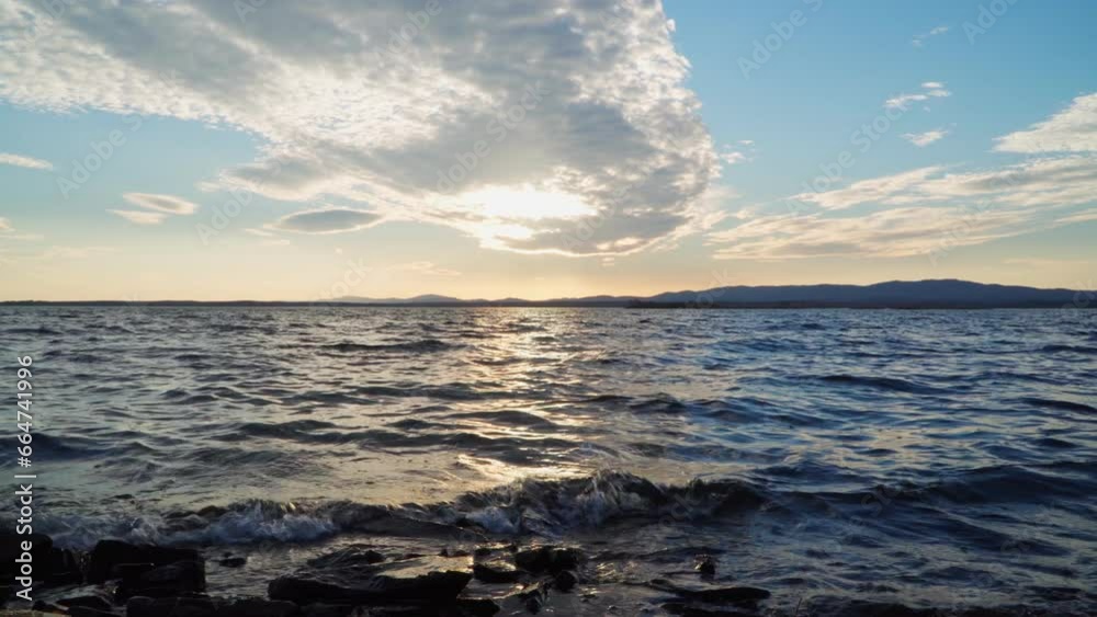 Beautiful landscape on the shore of the lake. Movement of coastal waves. The clouds in the sky are illuminated by the bright sun. Beautiful landscape on the shore of the lake. Movement of coastal waves. The clouds in the sky are illuminated by the bright sun.
